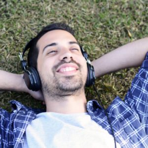 Man smiling, listening to music on grass.