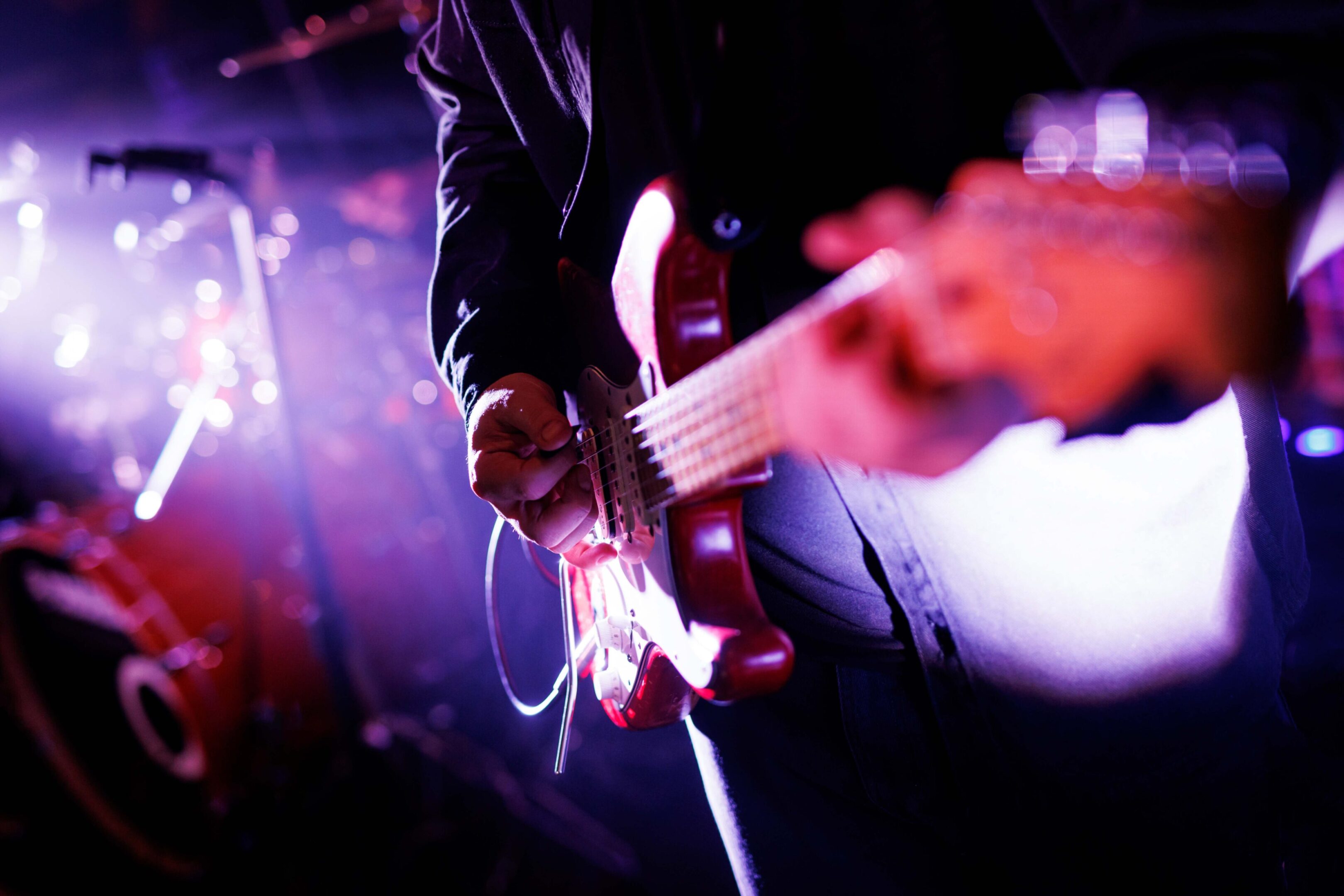 Close-up of musician playing electric guitar on stage with vibrant lighting.