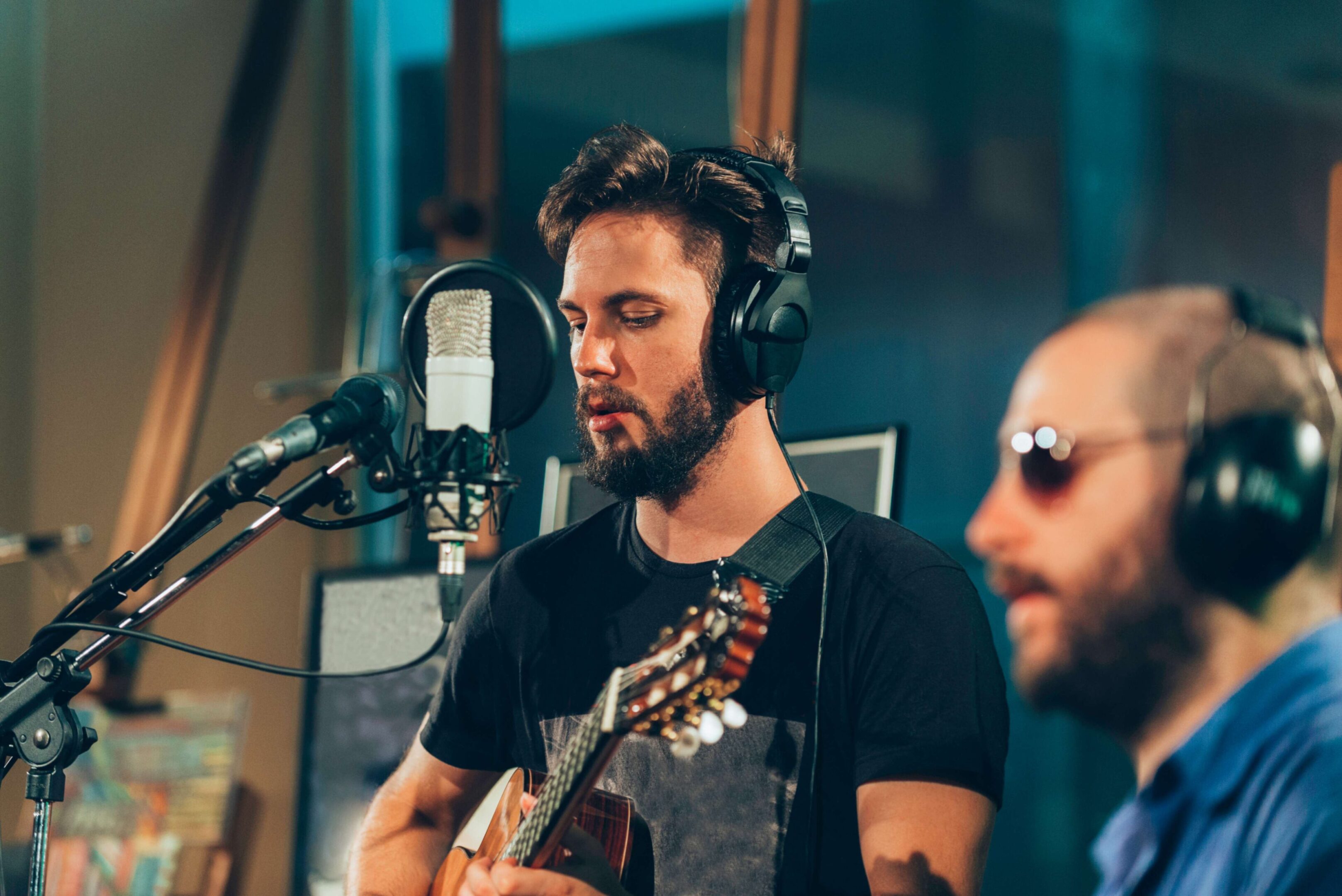 Musician singing and playing guitar in a recording studio with headphones on.